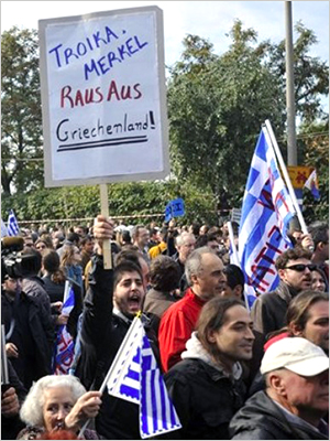 An anti-austerity protester carries a banner that reads in German,Troika-Merkel, out of Greece!